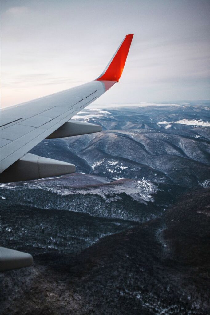 Scenic aerial view of a mountain range covered in snow, seen from an airplane wing.